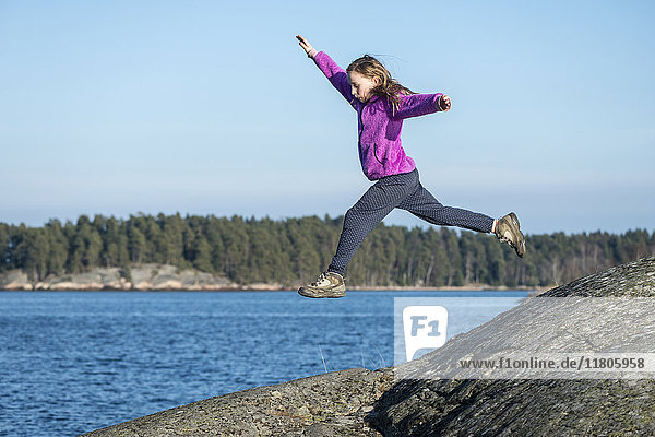 Girl jumping on rocky coast