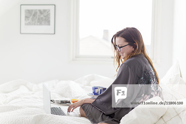 Junge Frau im Bett mit Laptop