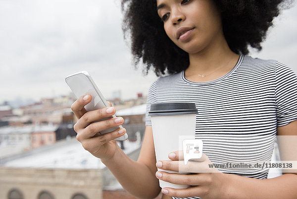 African American woman drinking coffee and texting on cell phone