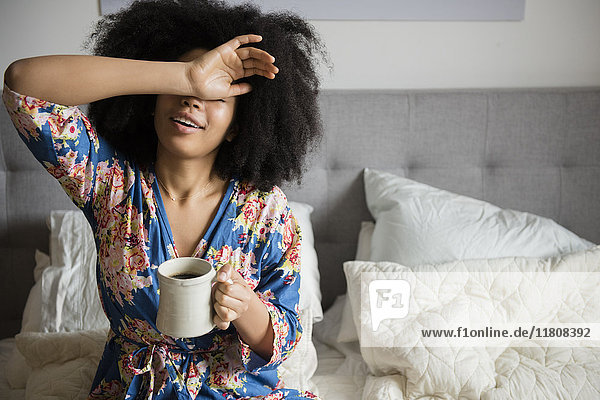Afroamerikanische Frau sitzt im Bett und trinkt Kaffee