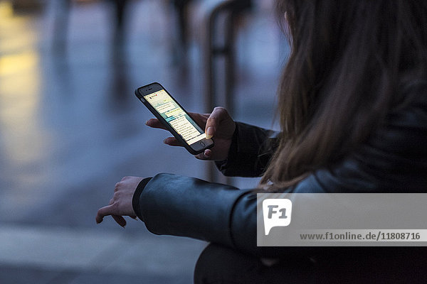 Kaukasische Frau  die im Freien eine SMS auf einem Mobiltelefon schreibt