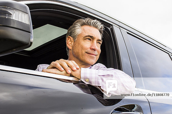 Lächelnder kaukasischer Geschäftsmann  der sich an ein Autofenster lehnt