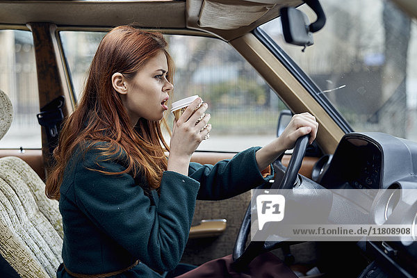 Wütende kaukasische Frau fährt Auto und trinkt Kaffee