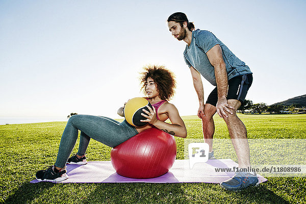 Paar trainiert mit Fitnessball und schwerem Ball in einem sonnigen Feld