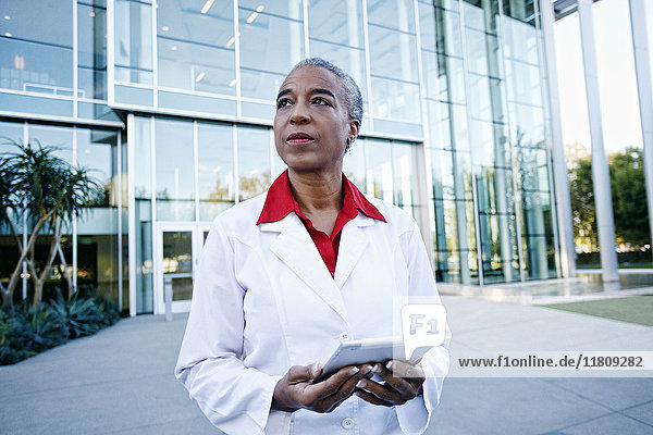 Portrait of serious African American doctor holding digital tablet outdoors