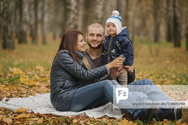 Middle Eastern couple sitting in park with baby son in autumn
