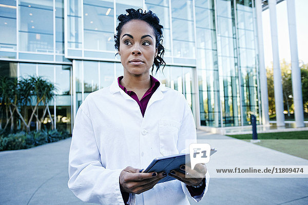 Portrait of curious Mixed Race doctor holding digital tablet outdoors