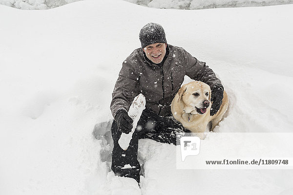 Caucasian man sitting in snow hugging dog