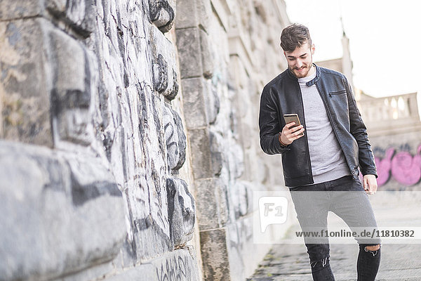 Lächelnder kaukasischer Mann  der auf dem Bürgersteig geht und eine SMS auf seinem Handy schreibt