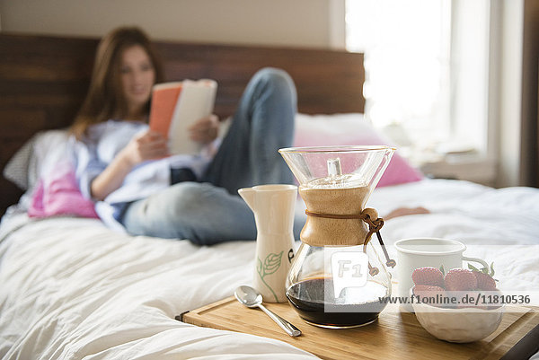 Kaukasische Frau liegt im Bett und liest ein Buch neben dem Frühstückstablett