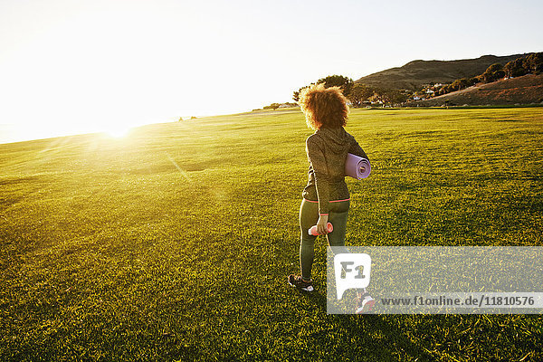 Hispanic woman carrying exercise mat in sunny field