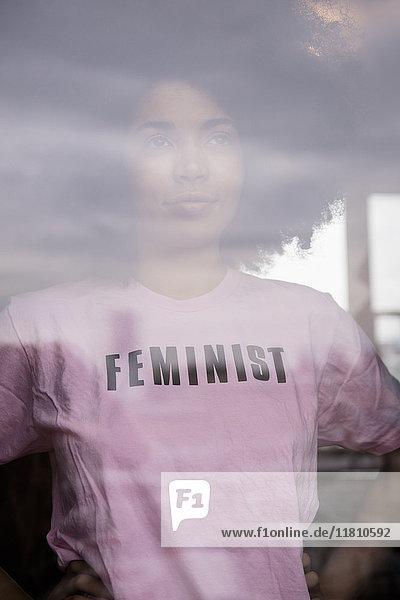 Afroamerikanische Frau mit feministischem T-Shirt hinter dem Fenster