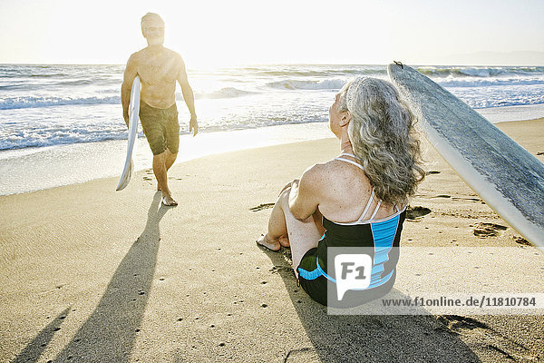 Older Caucasian couple on beach with surfboards