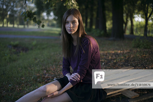 Serious Caucasian woman sitting on wooden pallet in park