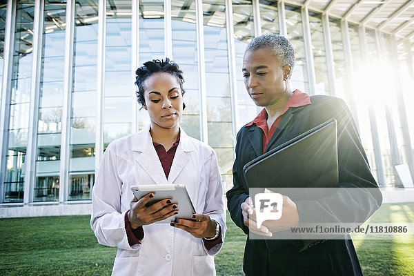 Doctor and administrator outdoors at hospital using digital tablet