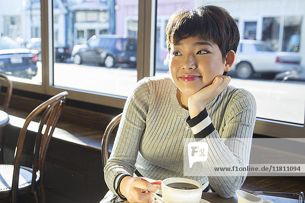 Pensive Asian teenage girl drinking coffee in coffee shop
