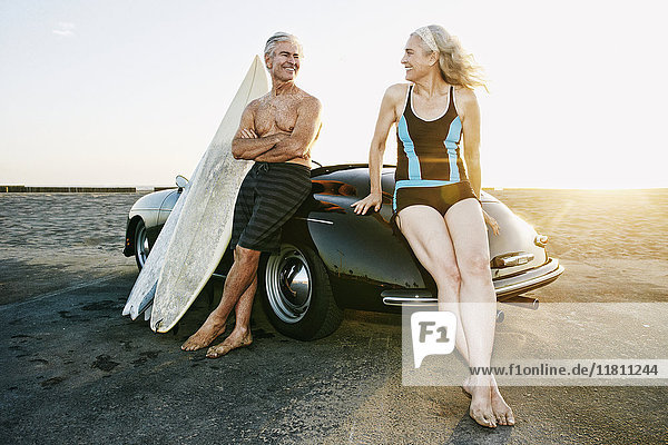 Älteres kaukasisches Paar lehnt sich mit Surfbrettern an ein Cabrio