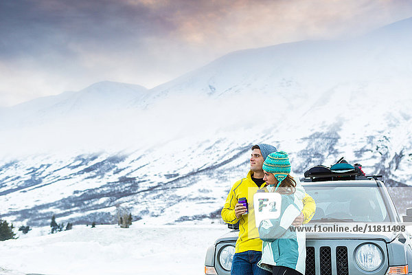 Kaukasisches Paar  das sich im Winter umarmt und an ein Auto lehnt