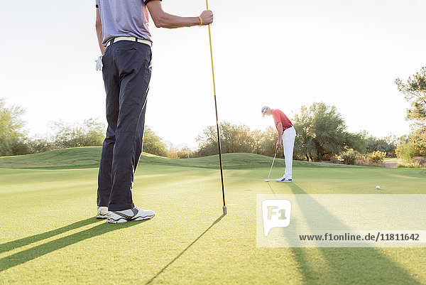 Hispanic man watching friend on golf course