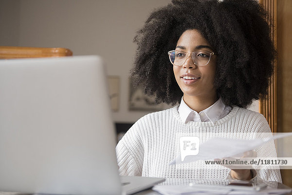 Afroamerikanische Frau hält Papierkram und benutzt einen Laptop