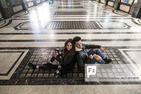 Kaukasisches Paar sitzt Rücken an Rücken auf dem Boden der Lobby