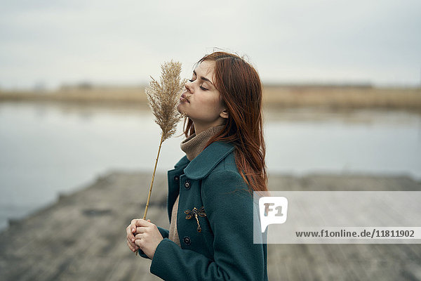 Caucasian woman standing on dock smelling stalk of grass