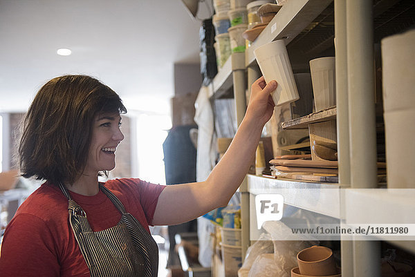 Lächelnde kaukasische Frau stellt Tasse auf Regal in Werkstatt