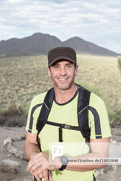 Porträt eines lächelnden hispanischen Mannes beim Wandern in der Wüste