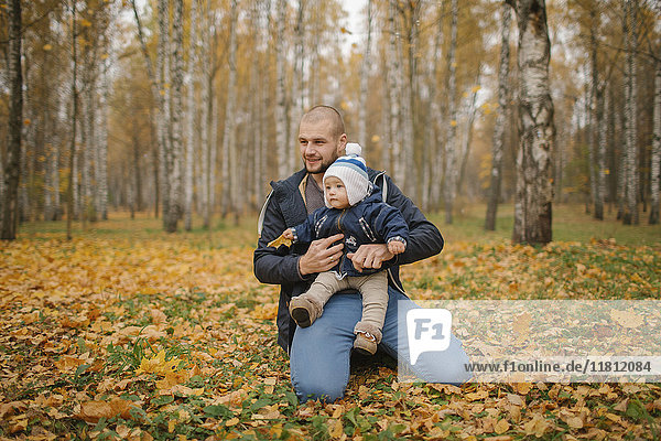 Vater aus dem Nahen Osten kniet im Park mit seinem kleinen Sohn im Herbst