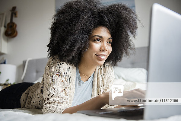 Afroamerikanische Frau liegt im Bett und benutzt einen Laptop