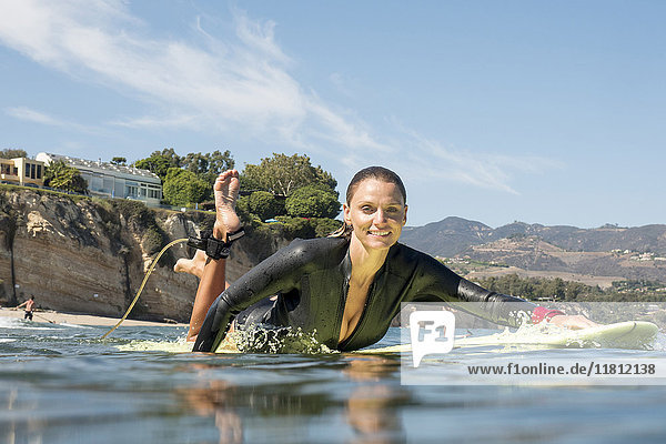 Lächelnde kaukasische Frau paddelt auf einem Surfbrett im Meer