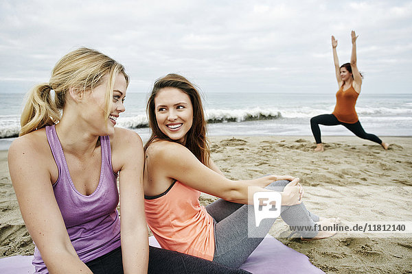 Kaukasische Frau macht Yoga am Strand in der Nähe von entspannenden Freunden