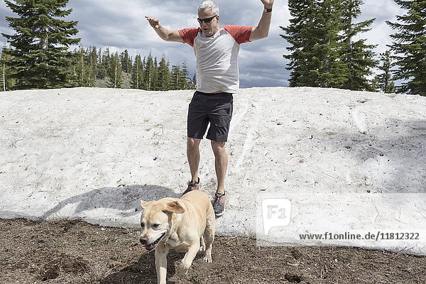 Kaukasischer Mann in kurzen Hosen rutscht mit Hund auf Schnee