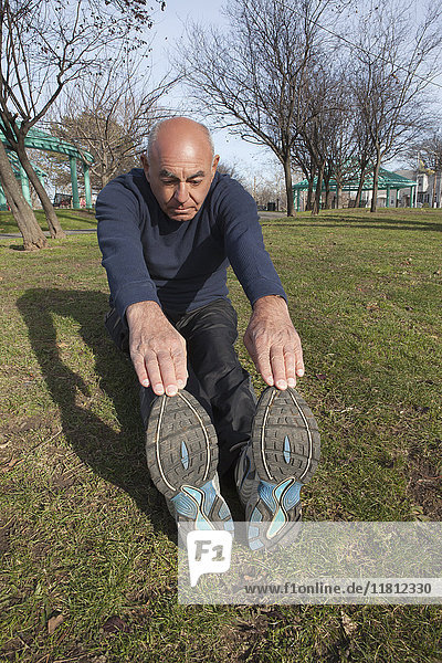 Hispanic man sitting on grass in park stretching legs