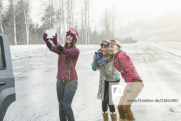 Women posing for cell phone selfie in winter using digital tablet