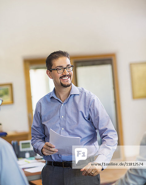 Lächelnder hispanischer Geschäftsmann  der Papierkram im Büro hält