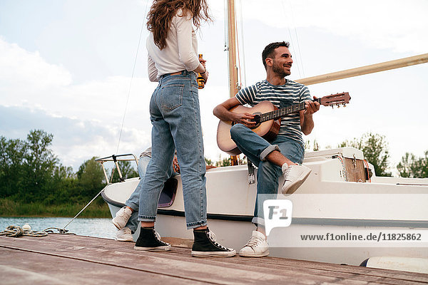 Drei Freunde entspannen sich am Pier  sitzen auf einem Segelboot  Mann spielt Gitarre