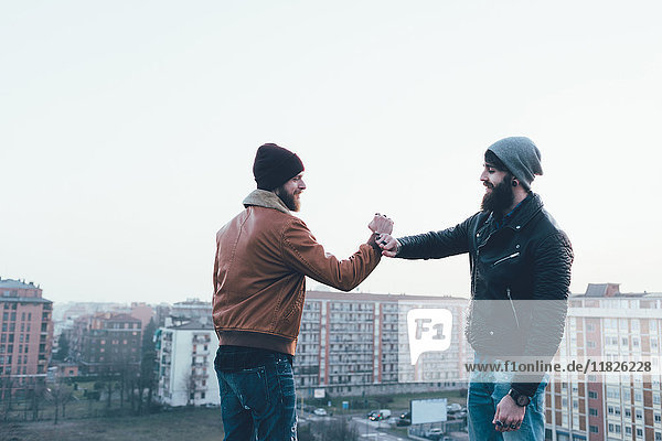Two young male hipsters fist bumping above cityscape