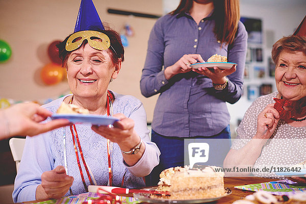 Ältere Frauen bekommen auf einer Party Geburtstagskuchen serviert