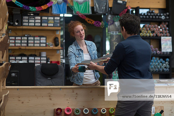Woman working in skateboard shop  handing skateboard to customer