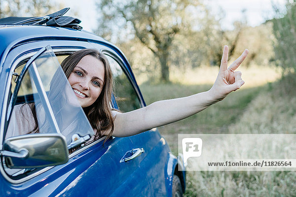 Frau schaut lächelnd aus dem Autofenster  Friedenszeichen  Firenze  Toskana  Italien  Europa