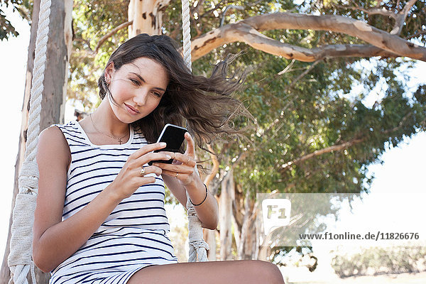 Young adult woman sitting on swing using smartphone