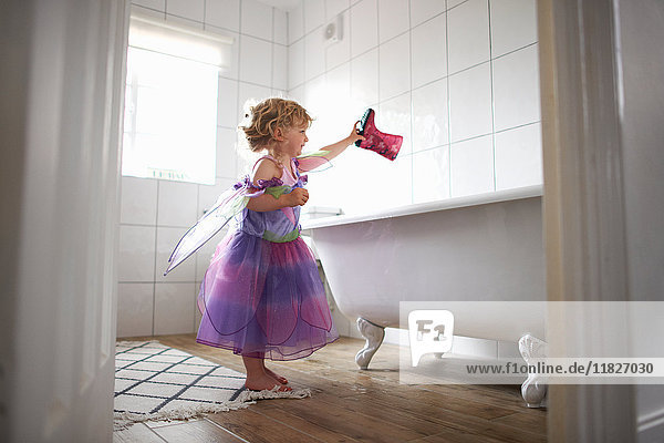 Junges Mädchen in Feenkostüm  hält Gummistiefel über die Badewanne