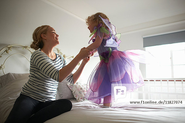 Young girl dressed in fairy costume  standing on bed  mother holding her hands