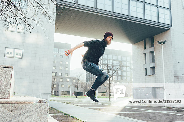 Junger männlicher Hipster springt in der Luft und übt Parkour in der Stadt