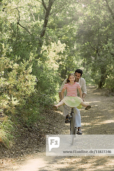 Father and daughter riding bicycle through forest