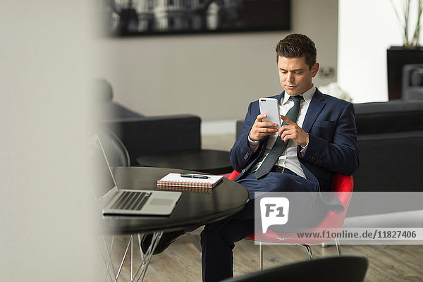 Businessman sitting in office looking at smartphone