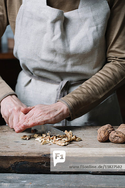Woman chopping walnuts on chopping board  using knife  mid section