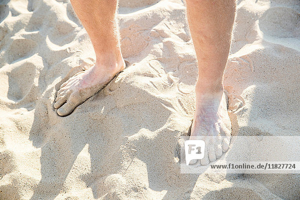 Nackte Füße und Knöchel eines jungen Mannes am trockenen Sandstrand stehend