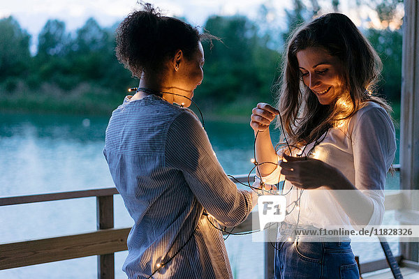 Zwei Frauen stehen sich gegenüber  beleuchtete Lichterketten um den Hals gewickelt  lächelnd